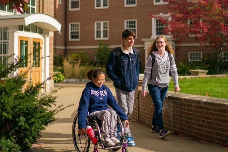 三个主要研究学生, 一个坐在轮椅上，两个站在她旁边, 在主要研究的穆克兰大厅的院子里散步和开车.