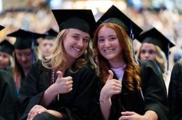 Two female 学生s give the thumbs up at commencement